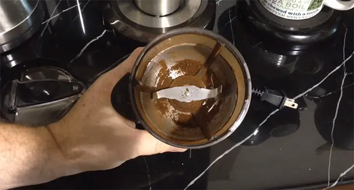 A dirty blade coffee grinder is shown by a barista. A lot of ground coffee stuck around the blade.