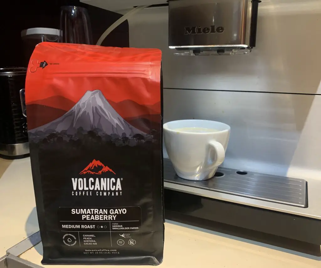Bag of Sumatran Gayo Peaberry coffee beans by Volcanica in front of bean to cup machine
